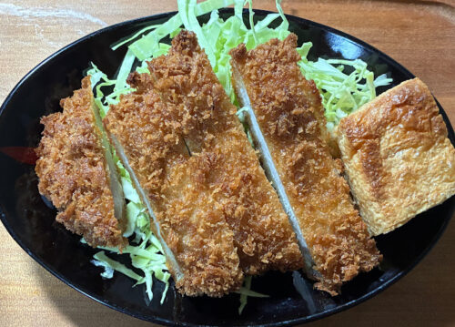 スーパーの惣菜トンカツを一人分のお皿に盛り付けた写真。節約しながら資産形成を続ける50代女性のリアルな食卓風景。